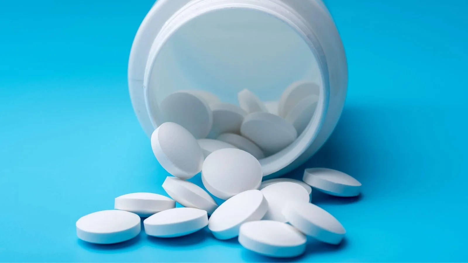 White tablets spilling out of an open medicine bottle onto a bright blue background, representing medication and Independent Prescribing in the UK.