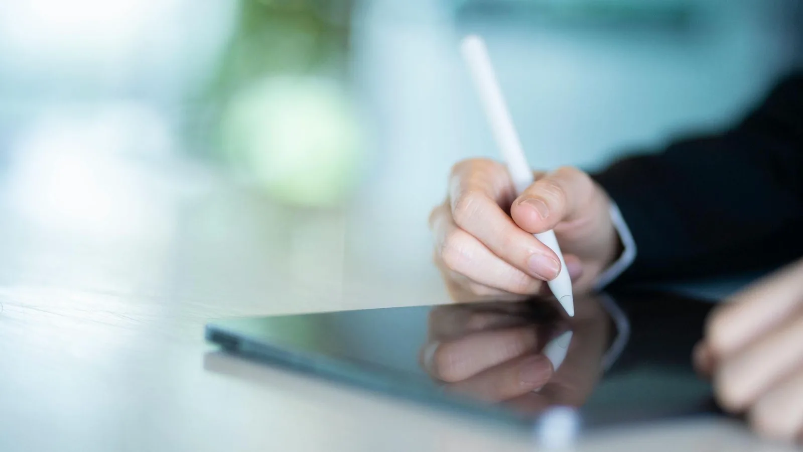 Close-up of a clinician's hand using a stylus on a digital device to complete medical documentation and prescribing records.